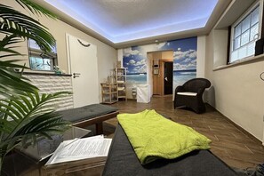 Een kamer met een bed, een stoel, een klein tafeltje, een plant en een muurschildering van de zee.