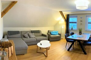 A modern living room with a sectional sofa, a round coffee table, and a dining table with chairs. - Holiday home "On the cliffs" - Apt. 5 (Boltenhagen Redewisch)
