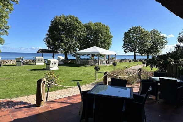 Een terras met tafels en stoelen, een overdekte veranda en uitzicht op zee.