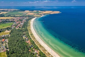 Luchtbeeld van een kustgebied met een strand, woongebouwen en een heldere blauwe zee.
