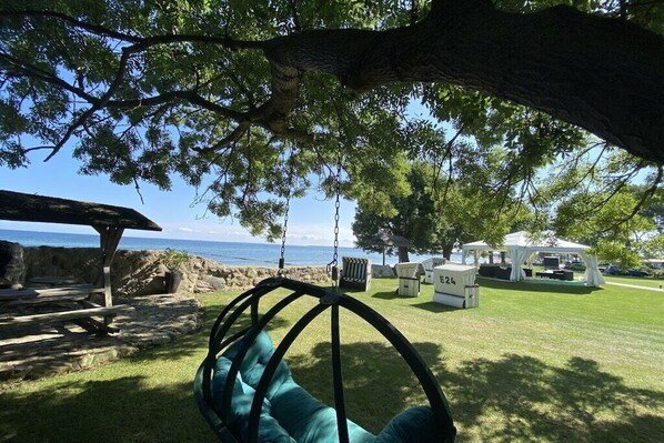Una silla colgante con vista al océano, una mesa de picnic y una zona con carpa y asientos.