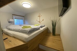 Een slaapkamer met een bed, nachtkastje, een aan de muur bevestigde televisie en een raam.