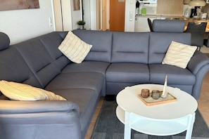 A grey sectional sofa with two pillows, a white coffee table with decorative items, and a grey rug. - Strandpalais Apt. 404 (Cuxhaven-Duhnen)