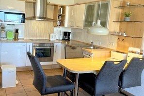 A compact kitchen with a stove, oven, microwave, and a small dining area with a table and chairs. - Strandpalais Apt. 404 (Cuxhaven-Duhnen)