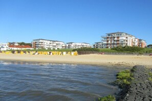A coastal hotel with multiple floors, a sandy beach in the foreground, and a clear sky. - Strandpalais Apt. 404 (Cuxhaven-Duhnen)