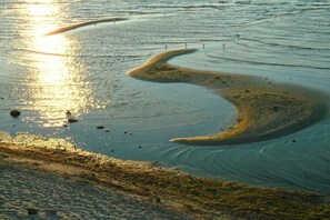 Een strand met een golvende zandformatie en rustig water.
