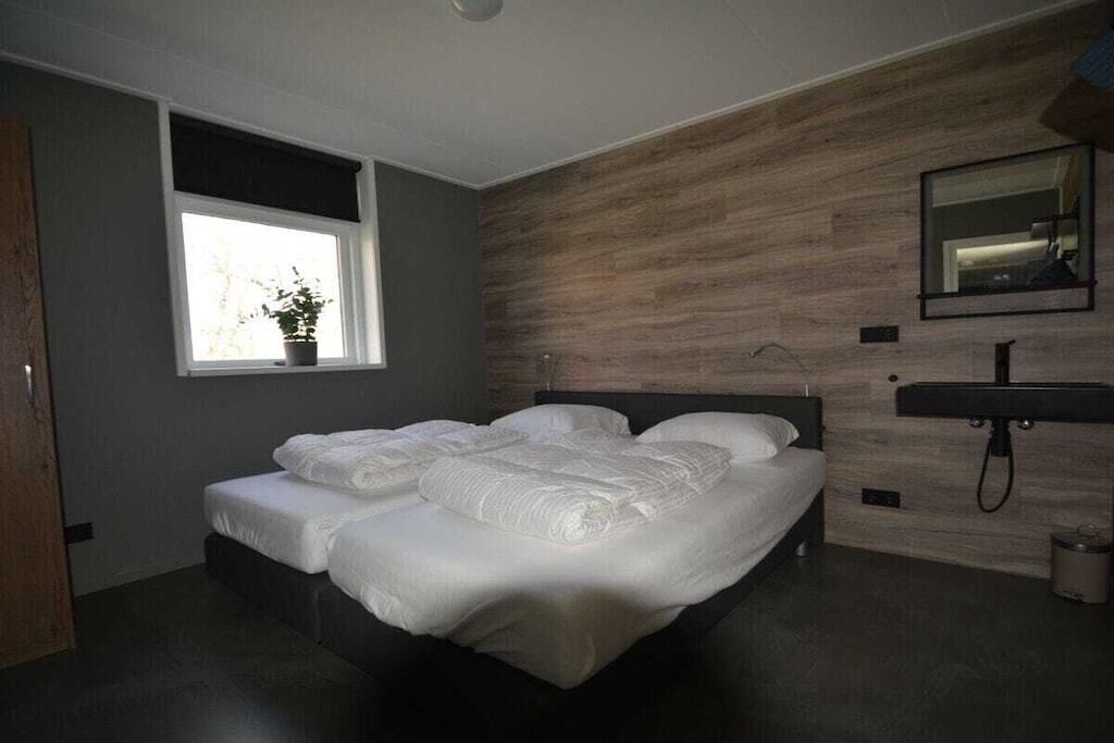 A modern bedroom with a bed, a window with a plant, a wooden wall, and a bathroom sink.
