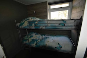 Een stapelbed met bloemen- en vlinderbeddengoed, een raam met uitzicht en een wandlamp.