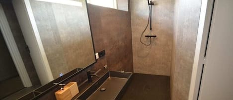 A modern bathroom with a large mirror, a black sink, and a shower area.