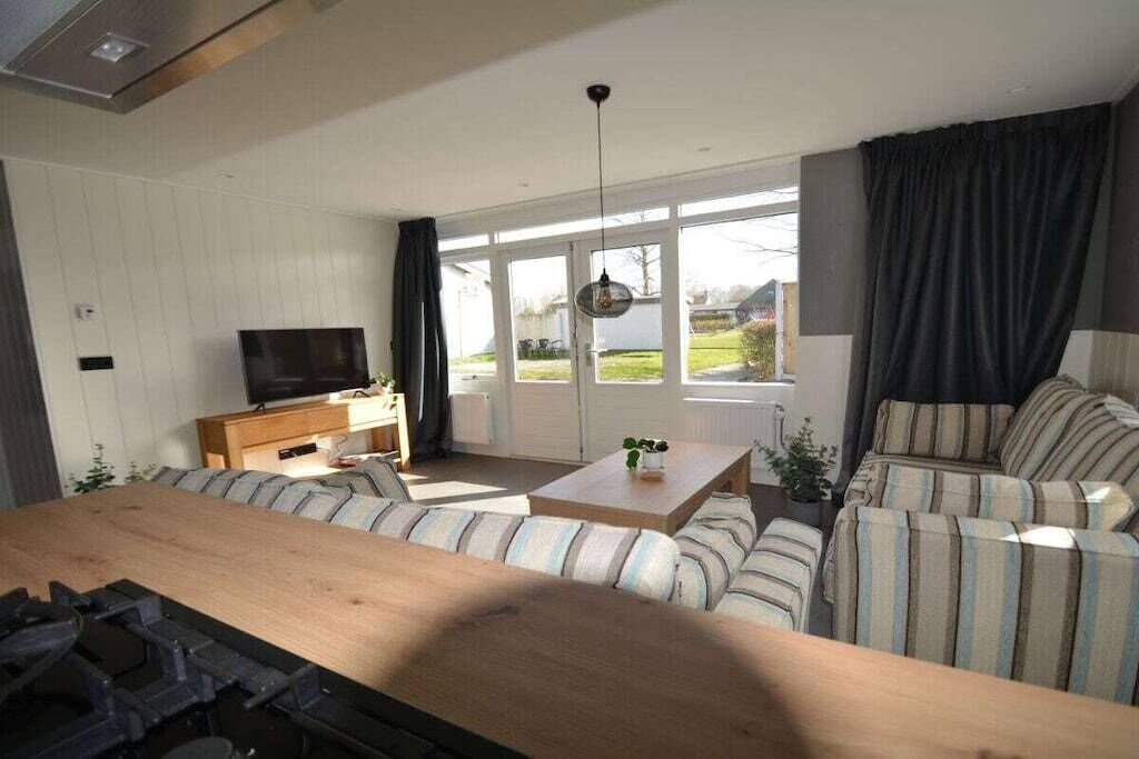 A modern living room with a sofa set, a coffee table, a television, and a large window with curtains.