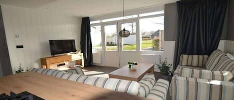 A modern living room with a sofa set, a coffee table, a television, and a large window with curtains.
