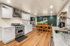 A modern kitchen with white cabinetry, a gas stove, an oven, and a dining area with wooden chairs and a table. - Tanglewood Tahoe Retreat (South Lake Tahoe)