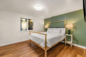 Ein Schlafzimmer mit einem Holzbettgestell, zwei Nachttischlampen, einem Fenster mit Blick auf Bäume und einer grünen Akzentwand.