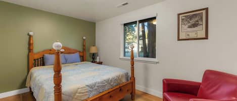 Un dormitorio con cama con dosel, una silla roja, una ventana con vista a árboles y un cuadro en la pared.