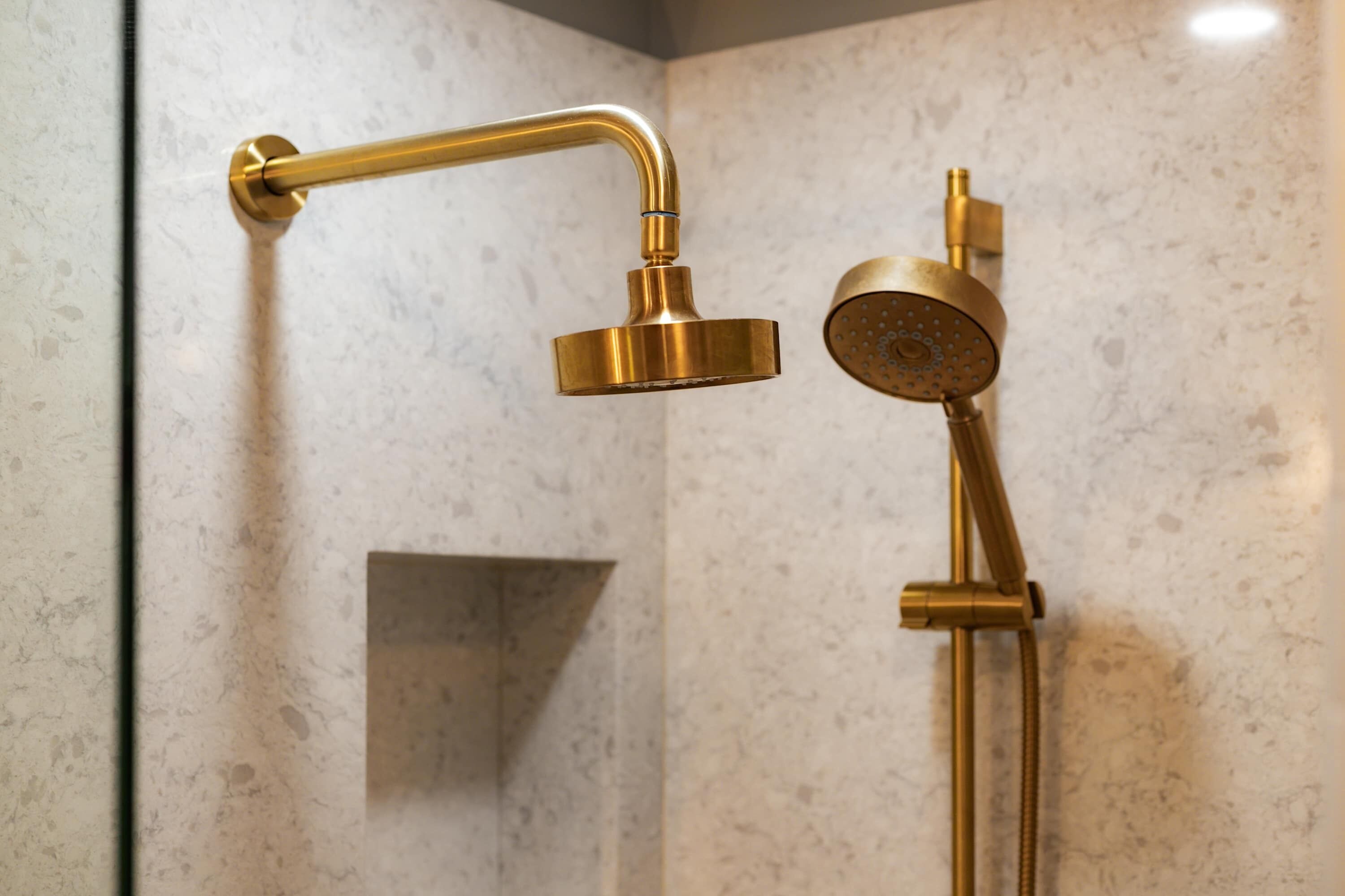 A bathroom with a gold-colored shower fixture mounted on a wall with a marble-like texture.