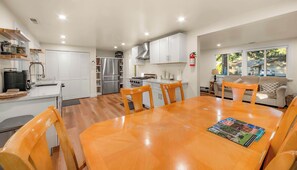 A modern kitchen with white cabinets, stainless steel appliances, and a dining area with a wooden table and chairs. - Tanglewood Tahoe Retreat (South Lake Tahoe)