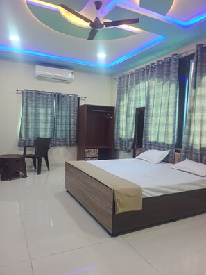 A bedroom with a bed, a ceiling fan, an air conditioner, and curtains. - The Arjun Palace By Elaichi Sirohi (Palri)