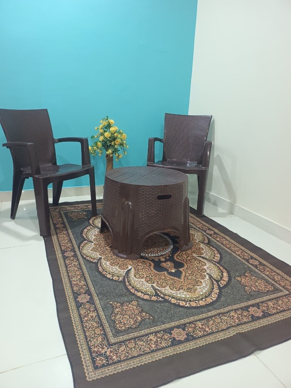 Una habitación con dos sillones oscuros de mimbre, una mesita redonda y un tapete estampado.