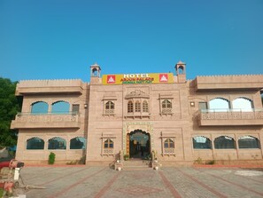 A large building with a prominent entrance, a sign indicating it is a hotel, and traditional architectural elements. - The Arjun Palace By Elaichi Sirohi (Palri)