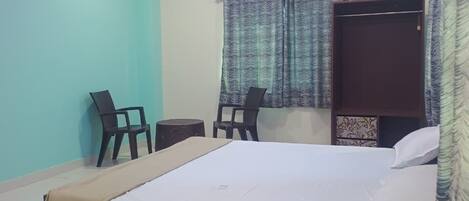 A bedroom with a bed, two chairs, an air conditioner, and a ceiling fan.