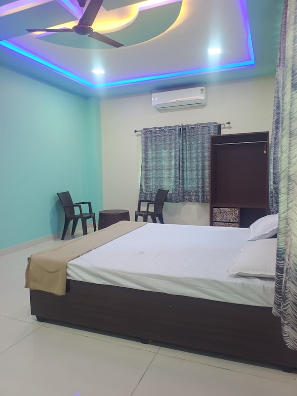 Un dormitorio con una cama, dos sillas, aire acondicionado y ventilador de techo.