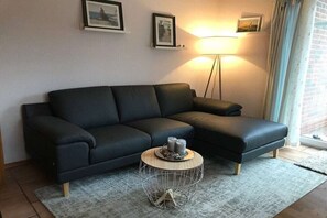 Ein Wohnzimmer mit einem schwarzen Sofa, einem runden Couchtisch mit Drahtgestell und einer Stehlampe.