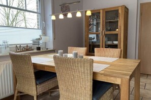 A dining area with a wooden table, wicker chairs, and a cabinet with glass doors. - Holiday home in Hooksiel with swimming pool (Hooksiel)