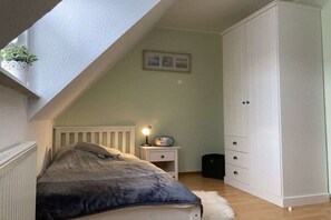 A bedroom with a bed, a nightstand, a lamp, a wardrobe, and a small plant. - Holiday home in Hooksiel with swimming pool (Hooksiel)