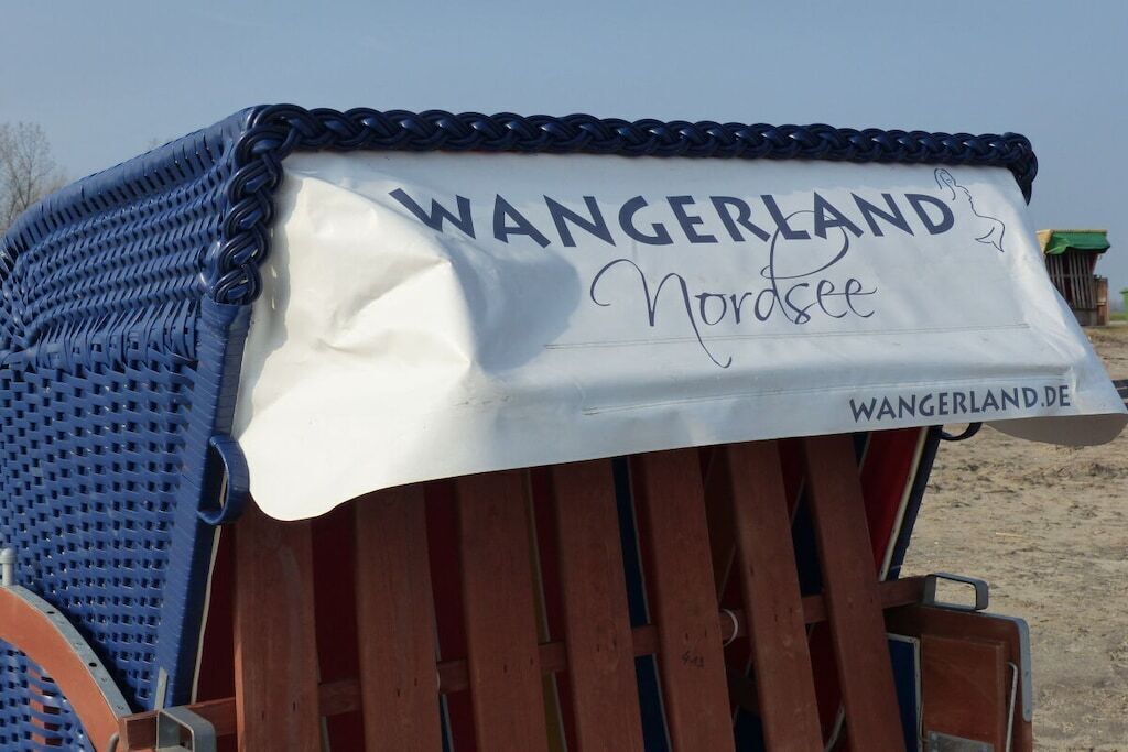 Una casetta sulla spiaggia con un cartello che recita 'WANGERLAND Nordsee' e il sito web 'WANGERLAND.DE'.
