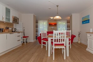 A modern kitchen with white cabinets, a microwave, and a dining area with a red sofa and white chairs. - Holiday apartment Villa Löwenstein 319577 (Kühlungsborn)