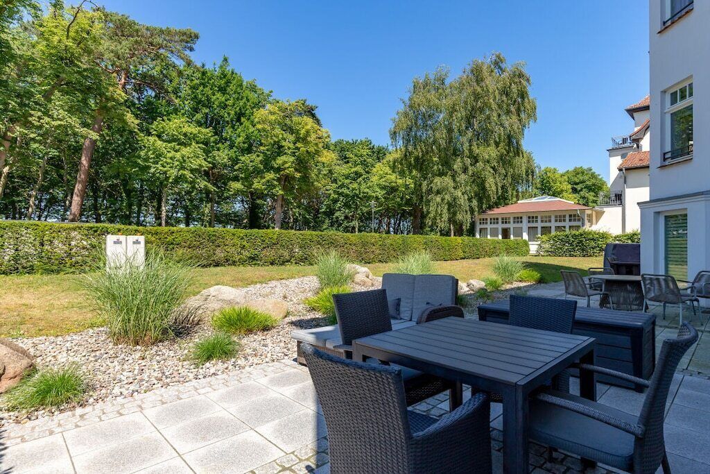 Ein Terrassenbereich im Freien mit Tisch und Stühlen, umgeben von einer Hecke und Bäumen.