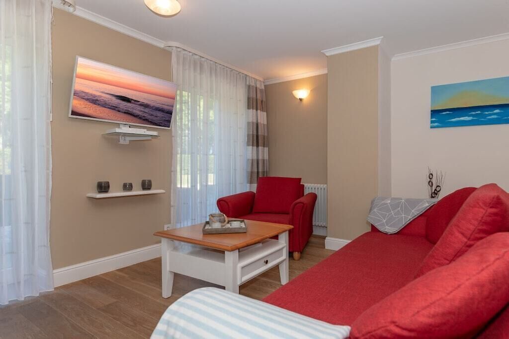Una sala de estar con un sofá rojo, un sillón rojo, una mesa de centro, un televisor montado en la pared y un cuadro.