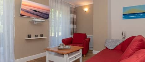 Una sala de estar con un sofá rojo, un sillón rojo, una mesa de centro, un televisor montado en la pared y un cuadro.