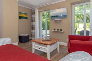A room with a bed, a red sofa, a wooden table, and a window with a view of greenery. - Holiday apartment Villa Löwenstein 319577 (Kühlungsborn)