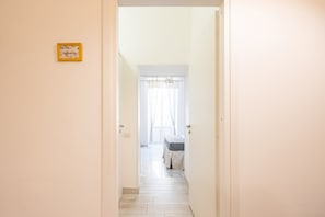 Een gang die uitkomt in een slaapkamer met een bed en een raam met gordijnen.