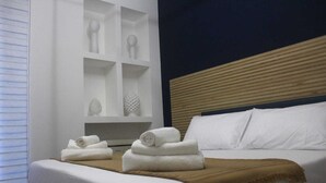 Una habitación de hotel con cama, cabecera, repisa con adornos y ventana con persianas.