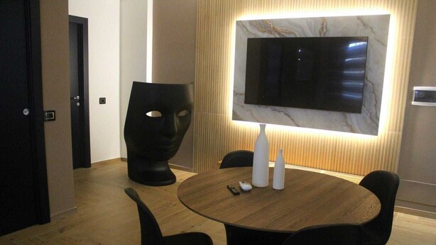 Un comedor moderno con una mesa redonda, sillas negras, un televisor montado en una pared de mármol y una escultura negra original.