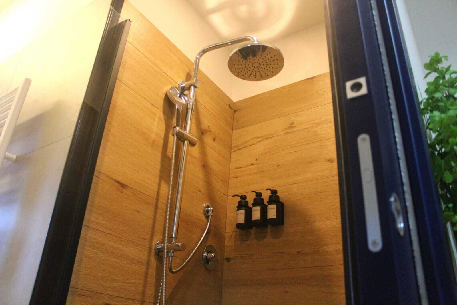 Un box de ducha de madera con un cabezal de ducha manual y un grifo empotrado.
