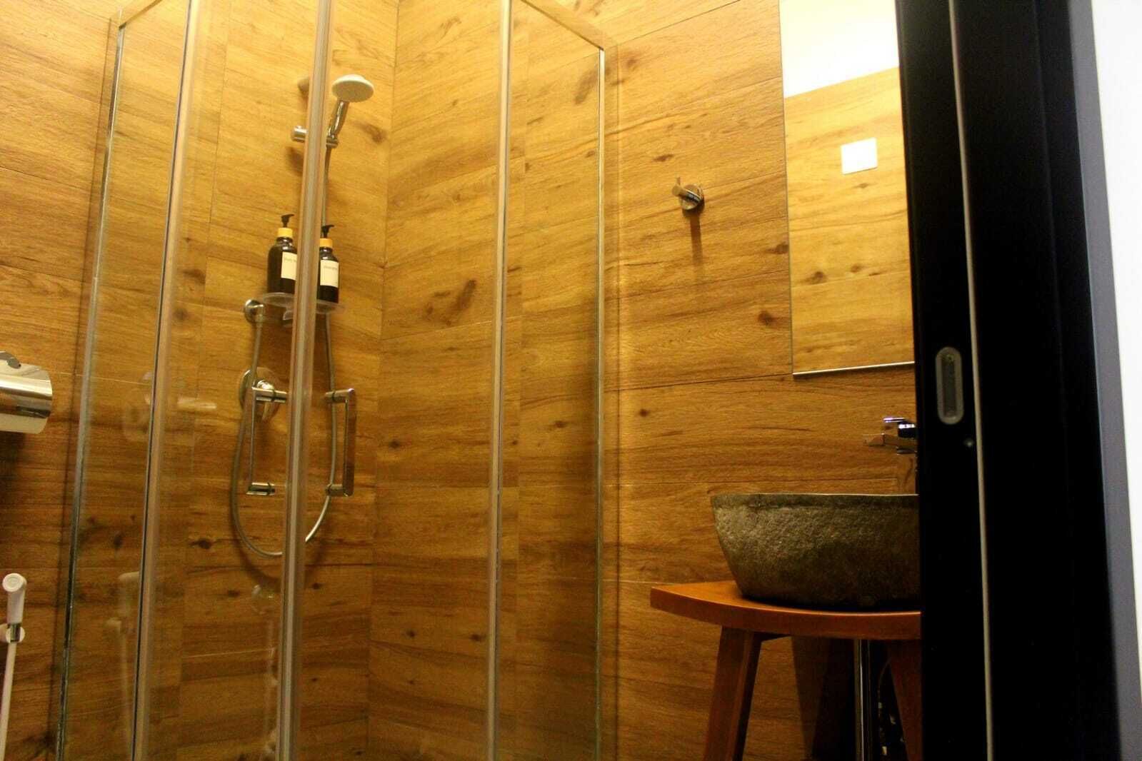 Eine Duschkabine mit Holzauskleidung, einer Glastür, einer Handbrause und einem Seifenspender.