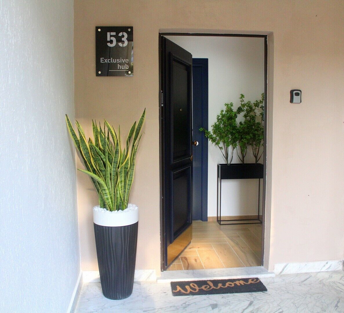 A hotel entrance with a welcome mat, a potted plant, and a door with a number sign.