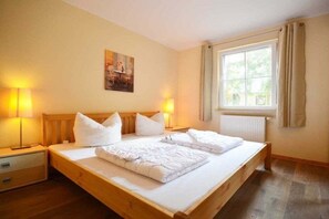 Een hotelkamer met een houten bed, twee bedlampen, een raam met gordijnen en een schilderij aan de muur.