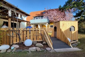Ein hölzernes Spielhaus mit einer Rampe, umgeben von einem Holzzaun und Steinen.