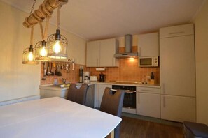 A compact kitchen with a dining table, chairs, a stove, microwave, and hanging light fixtures. - Holiday apartment with 2 bedrooms (Kölpinsee \/ Loddin)