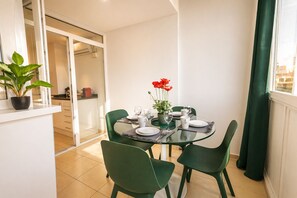 A dining area with a glass table, green chairs, and a potted plant with red flowers. - Nogalera Privée - Adults Only (Torremolinos)