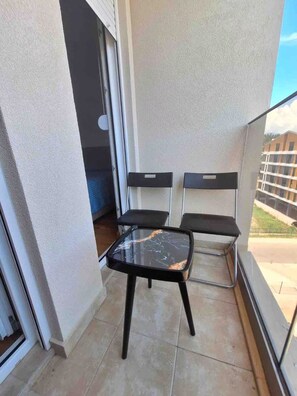 A balcony with a table and two chairs, a sliding glass door, and a view of buildings. - Modern 1 bedroom - Free Street Parking - Self Check In - AC (Podgorica)