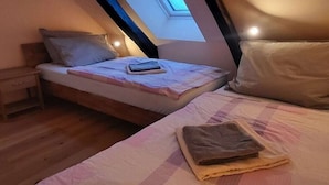 Quarto com teto inclinado, claraboia, cama com almofadas e mesa de cabeceira.