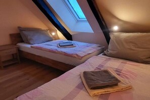 Ett sovrum med ett sluttande tak, ett takfönster, en säng med kuddar och ett sängbord.