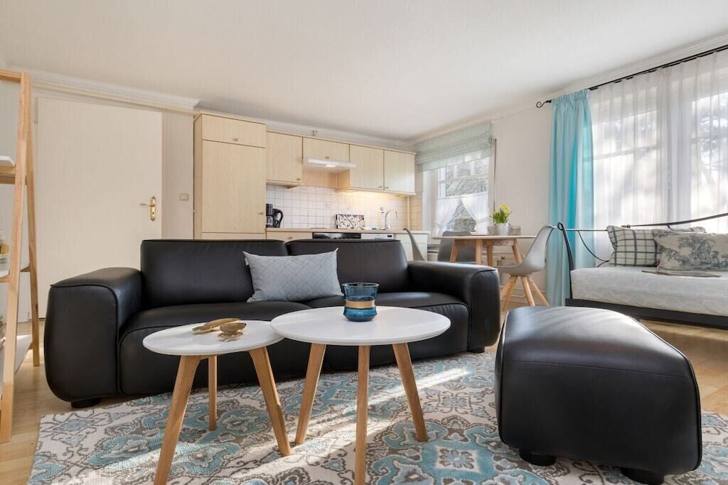 A modern living room with a black leather sofa, two white round tables, and a black ottoman.