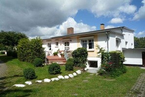 A two-story house with a front porch, a chimney, and a garden with a paved pathway. - Holiday apartment in Binz with swimming pool (Binz)