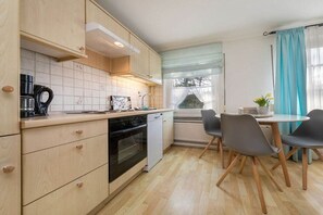 A compact kitchen with wooden cabinets, a dishwasher, and a dining area with a table and chairs. - Holiday apartment in Binz with swimming pool (Binz)